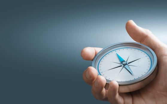 Hand holding a compass with a grey blue background.