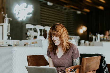 Woman smiling at a cafe, while sitting in front of her laptop.