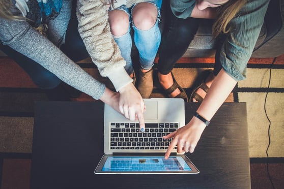 People sitting around a laptop, multiple hands on the keyboard.