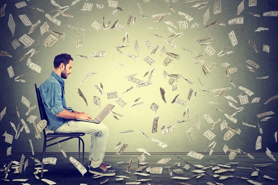 Young man using a laptop while dollar bills fly around him.